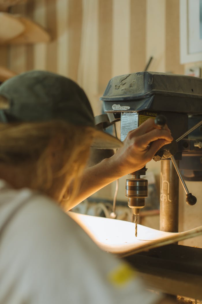 A craftsman working on a skateboard with a drill press in a woodcraft workshop.