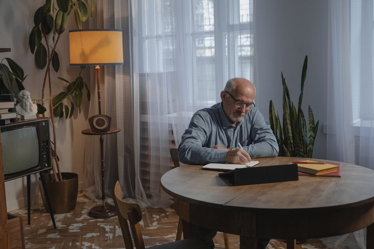 Senior man writing at home in a cozy setting with vintage decor and potted plants.