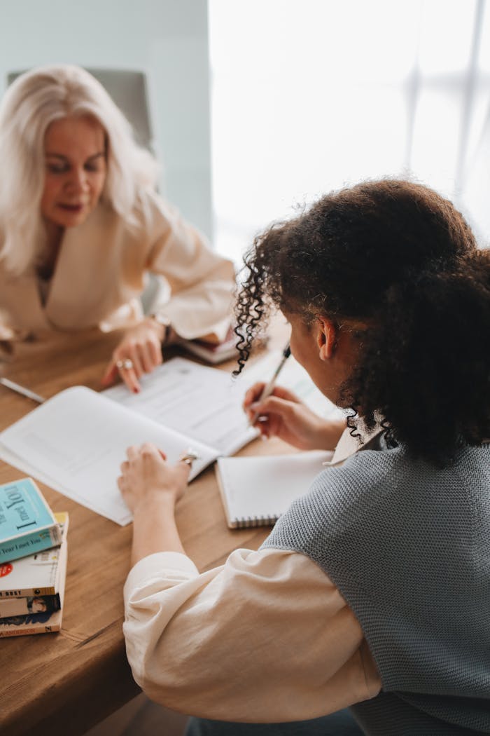 Two women engaged in discussion and study at a table with books and notepads.