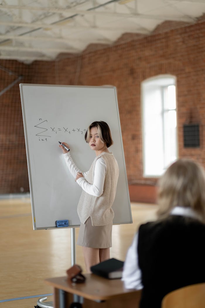 Female student presenting a math problem on a whiteboard in a classroom setting.