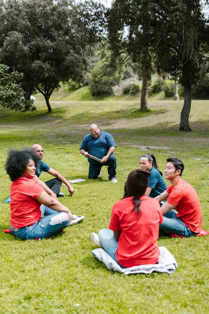 A diverse group of adults sitting in a circle outdoors, participating in a team building activity in a park.